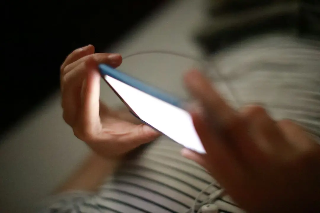 Två händer håller en mobil med tänd skärm i ett mörkt rum, som när du använder en IPTV-app med Toucan IPTV
