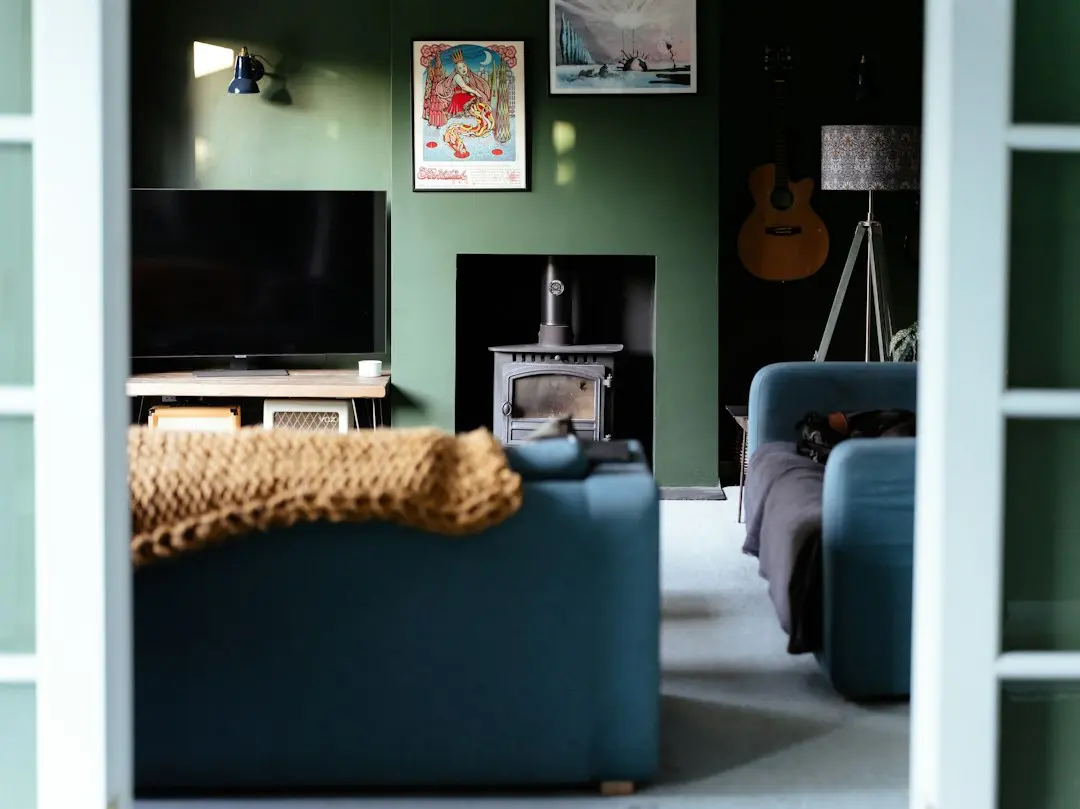 Ett vardagsrum med gröna väggar, en tv, en blå soffa och en kamin, sett genom en öppen dörr: här kan IPTV från Toucan IPTV ta plats